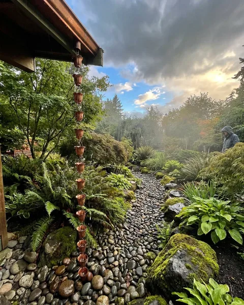 Copper rain chain beside a stone creek bed in a lush garden