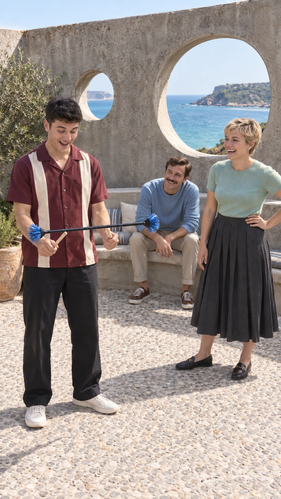 Three adult friends reacting to a flower stick balance on a seaside terrace with round openings framing blue water.