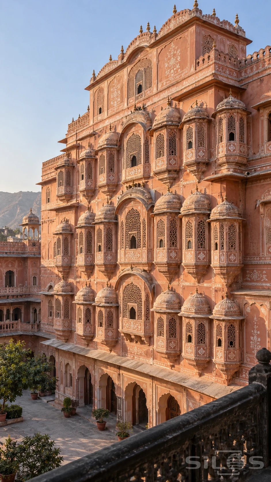 Rose-colored palace with tiers of domed lattice windows, pale floral borders and an empty stone courtyard.