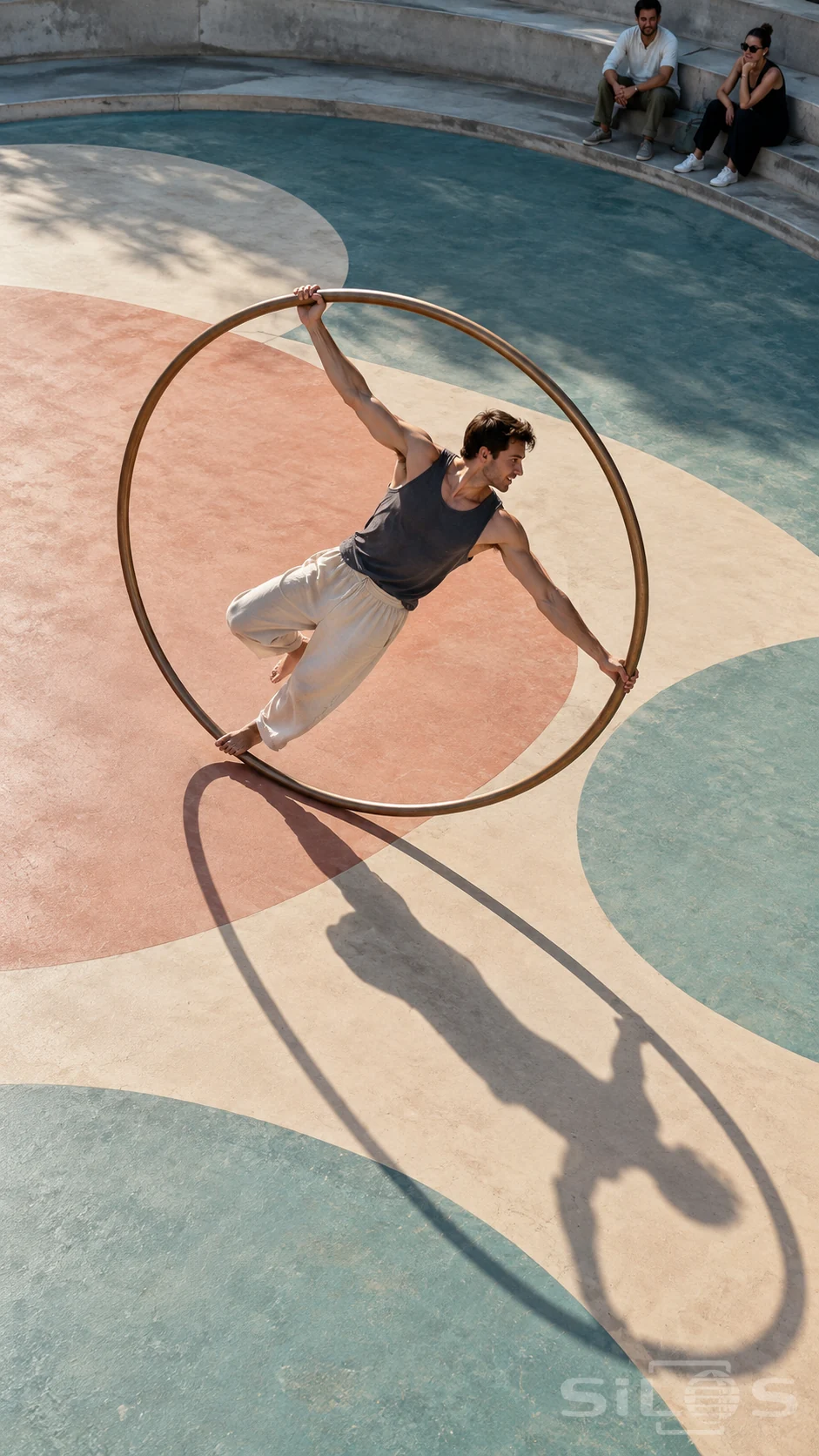 Cyr wheel performance with an adult athlete leaning inside a metal ring above painted circles and an elliptical shadow.