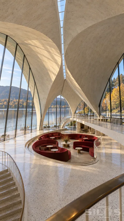 Grand glazed pavilion with wing-like ivory concrete roof shells; curved upper walkways and crimson sunken seating beside an autumn lake.