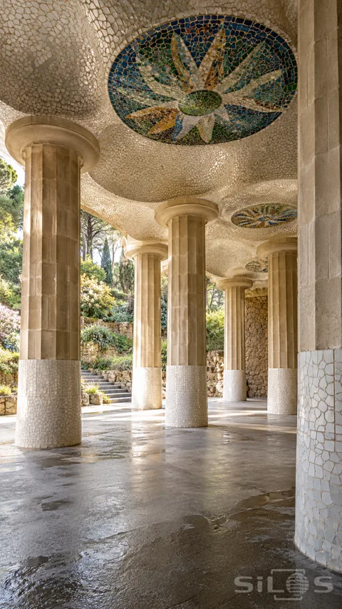 Fluted stone columns support an undulating ivory mosaic ceiling with blue; green and amber medallions above damp paving.