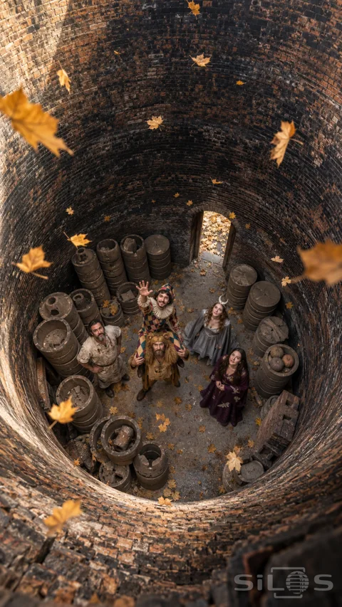 An overhead view into a brick kiln shows five costumed adults; one riding another’s shoulders; among clay saggars.