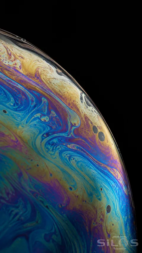 Iridescent soap film with flowing color bands; dark thinning patches and a curved film edge against a black background.