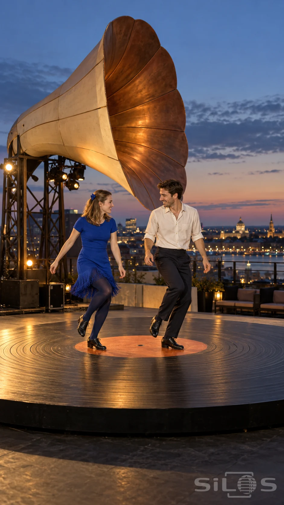 Two adults perform a tap duet on an enormous black record stage beneath a cream-and-copper horn above the city at dusk.