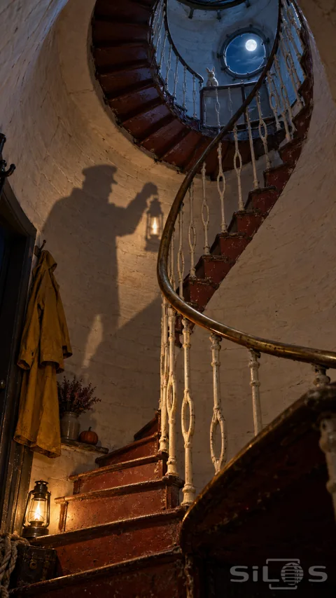 Worn red lighthouse stairs and white balusters wind upward to a porcelain hare beneath a moonlit porthole; with a keeper shadow on the wall.