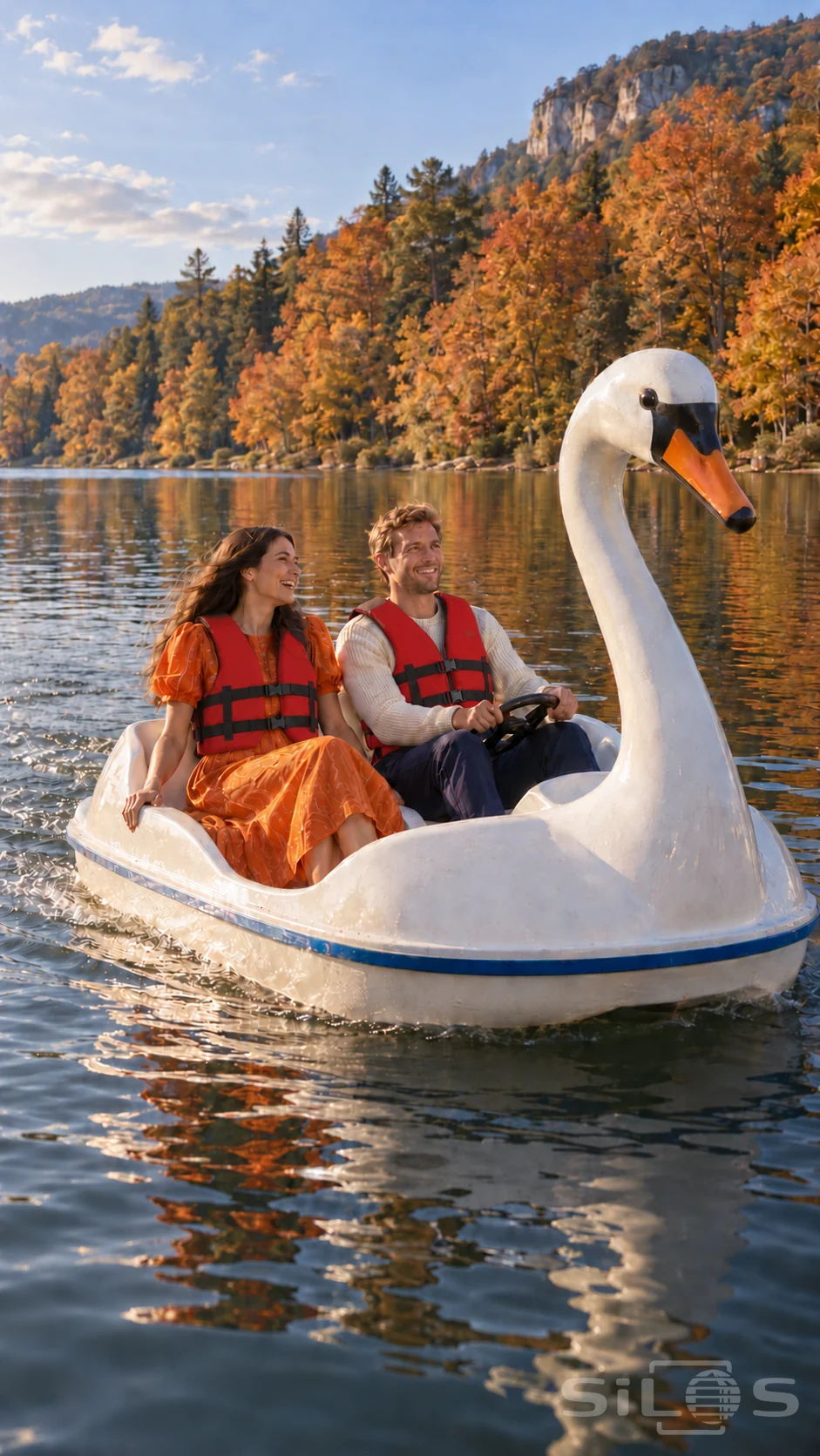 A laughing couple in red life jackets rides a white swan boat beside an autumn hillside.