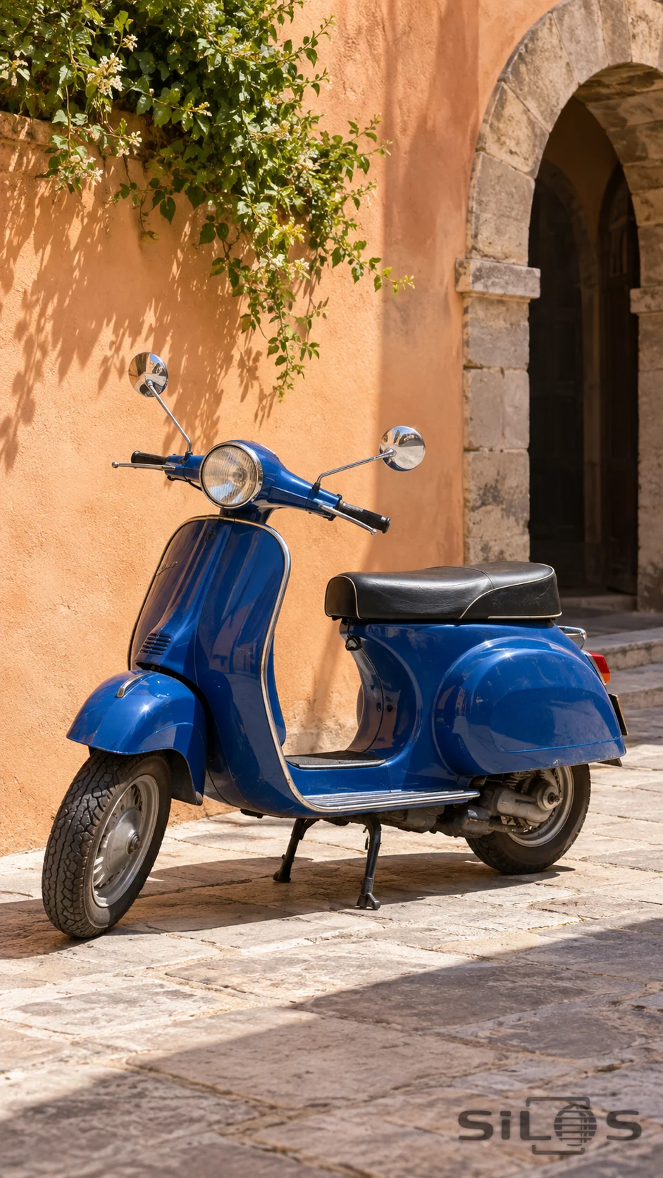 A cobalt-blue scooter rests in hard sunlight beside a peach-colored stone arch