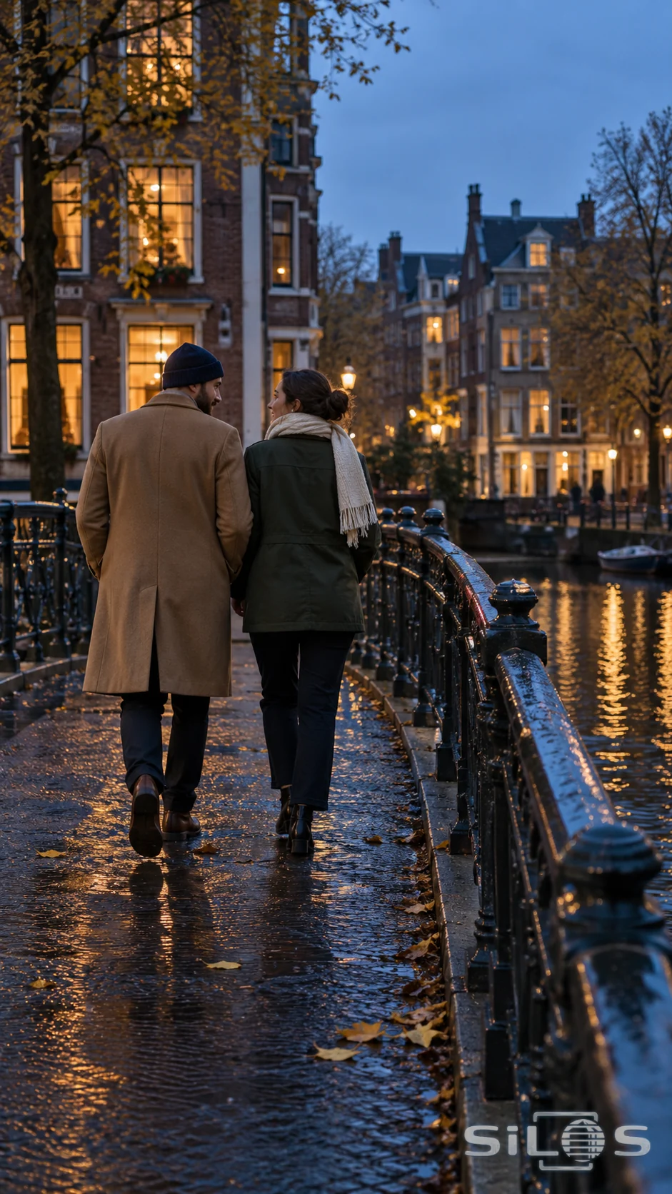 Two friends walk across a canal footbridge as city lights begin to glow
