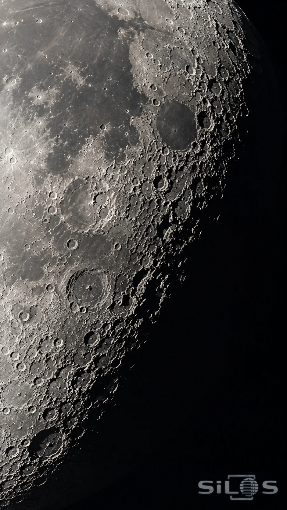 Rough lunar crater rims catch pale light beside a deep band of shadow