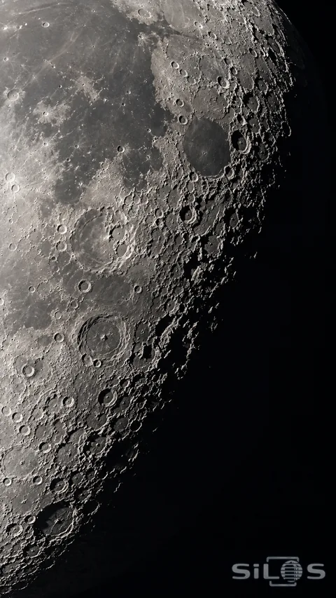 Rough lunar crater rims catch pale light beside a deep band of shadow