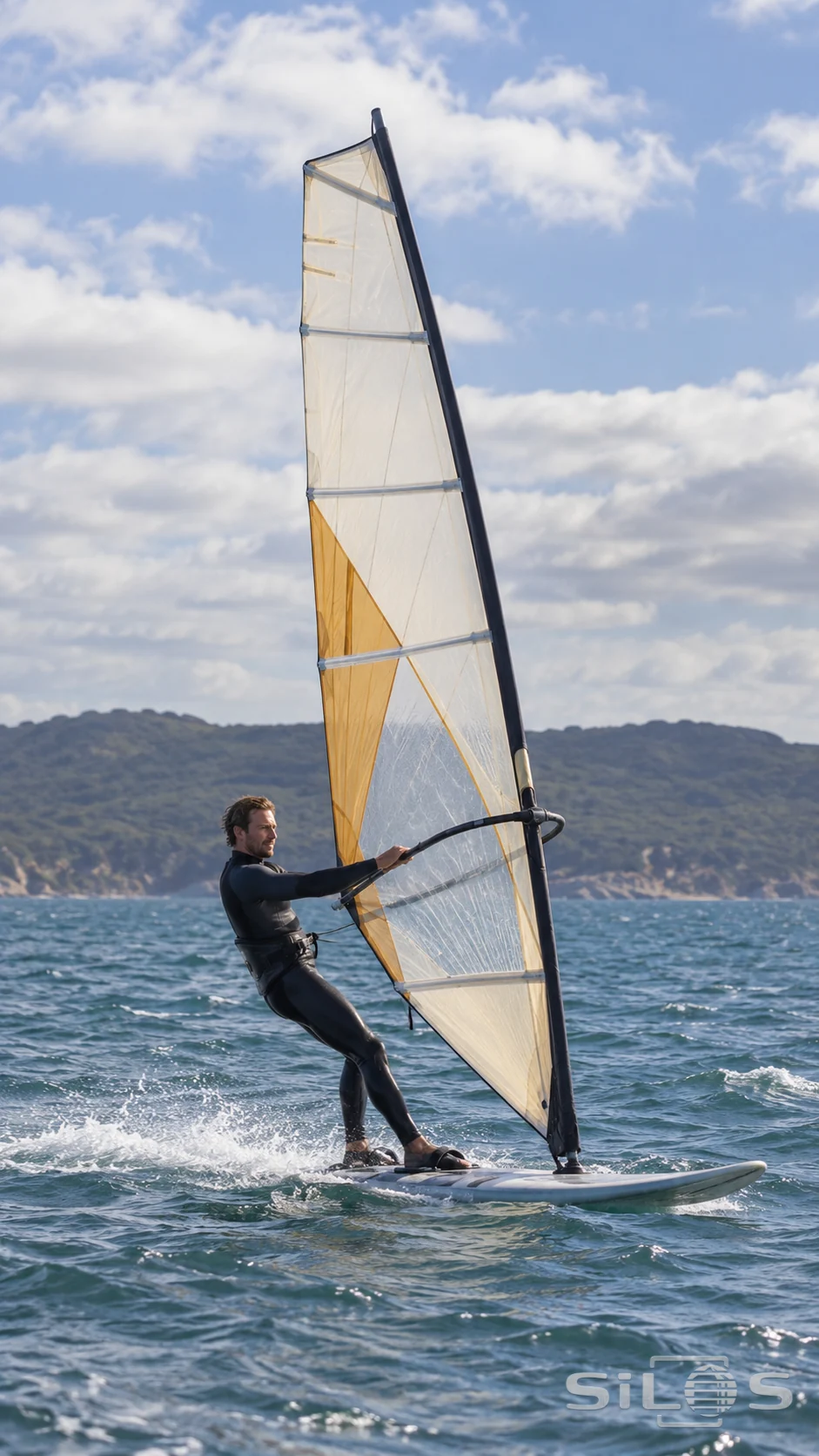 An adult windsurfer crosses a choppy bay with a full sail and board against a distant low coast.