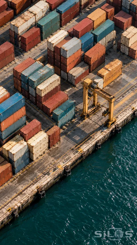 Weathered cargo containers form a colorful grid beside deep teal harbor water