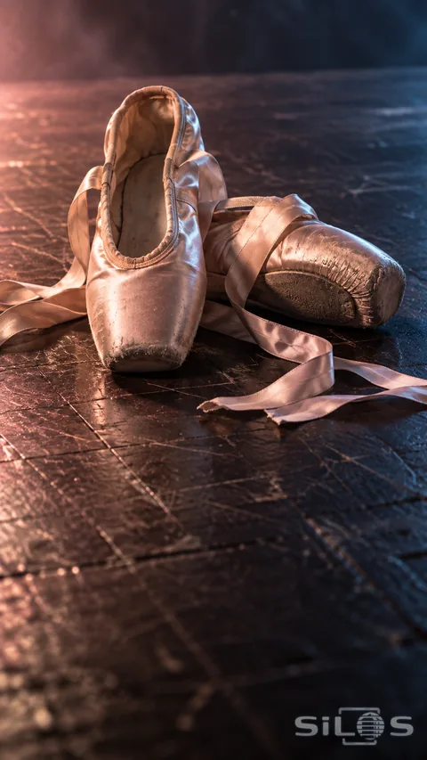 Pair of worn pale pink ballet pointe shoes with long satin ribbons on a dark wooden stage