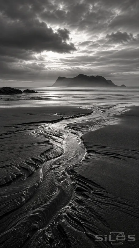 A winding tidal channel crosses dark wet sand toward a misty island and a bright opening in coastal cloud.