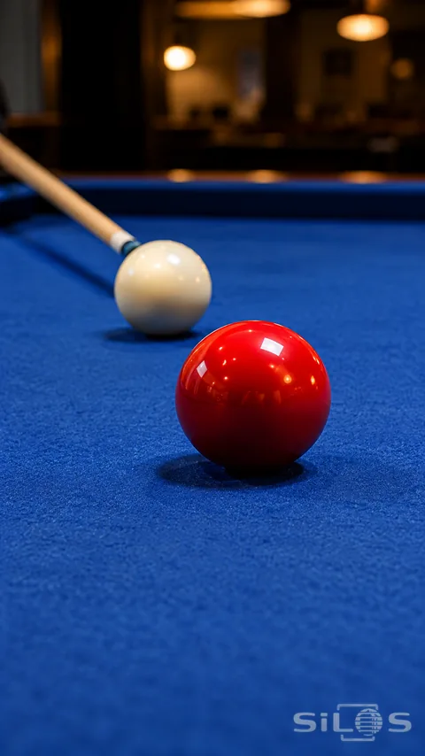 Red billiard ball in front of an ivory cue ball and maple cue on a deep blue table.