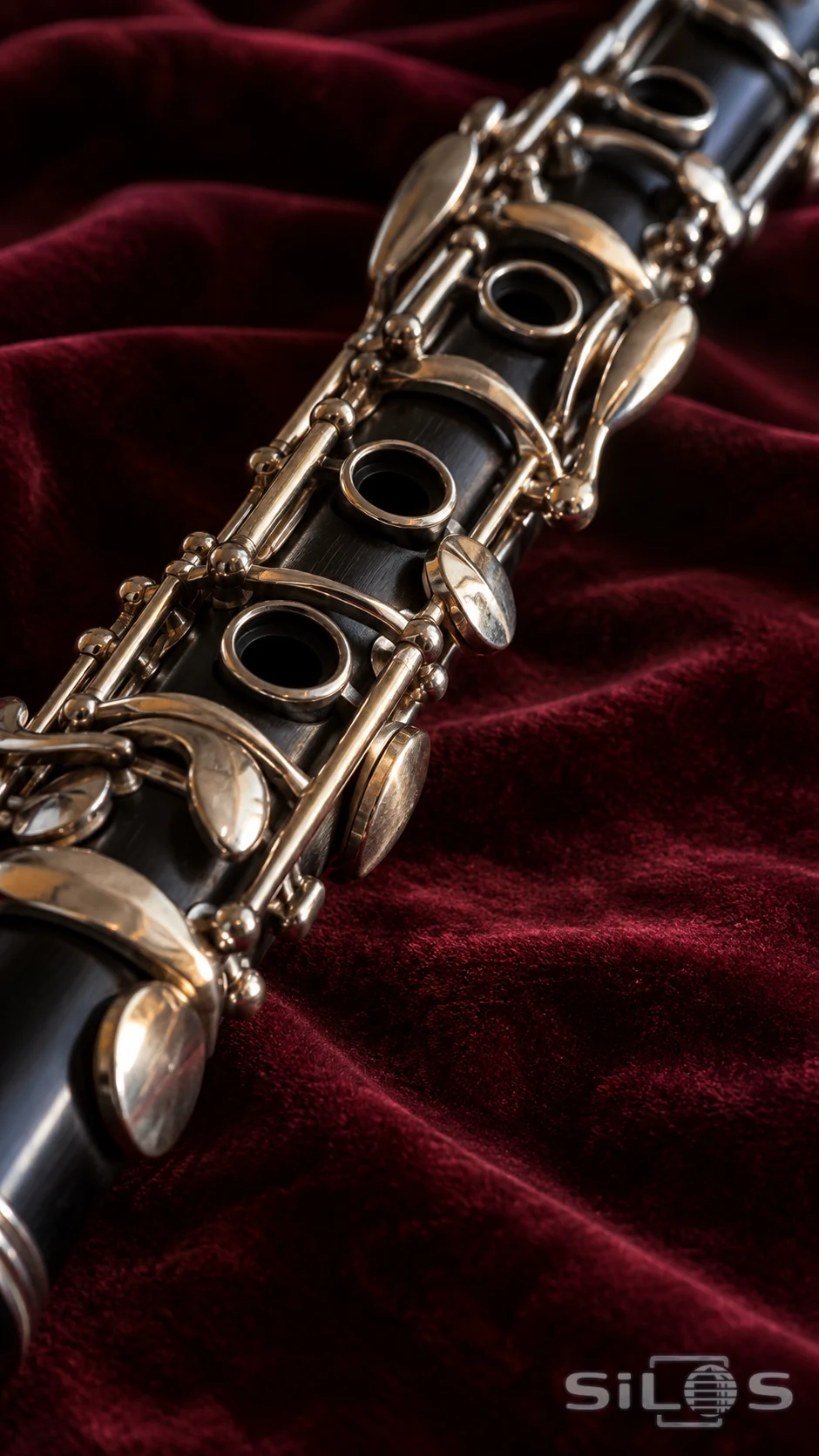 Close-up of silver clarinet keys and open tone holes against dark wood, resting diagonally on burgundy velvet