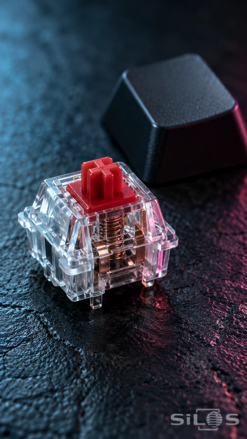 A transparent mechanical keyboard switch with a red stem and visible metal spring beside a plain dark keycap in cyan and magenta light.