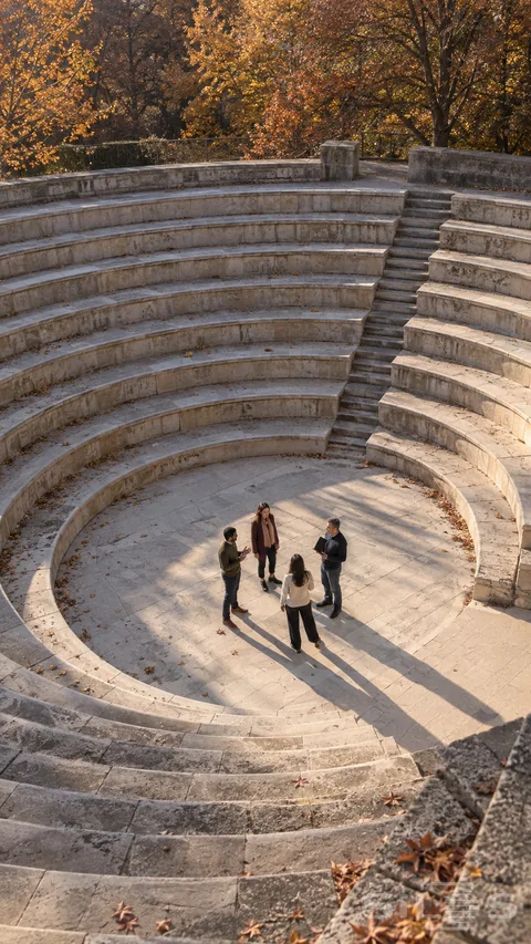 A high view shows four adults standing in a loose circle inside a curved stone amphitheater; with long shadows and bronze autumn trees.