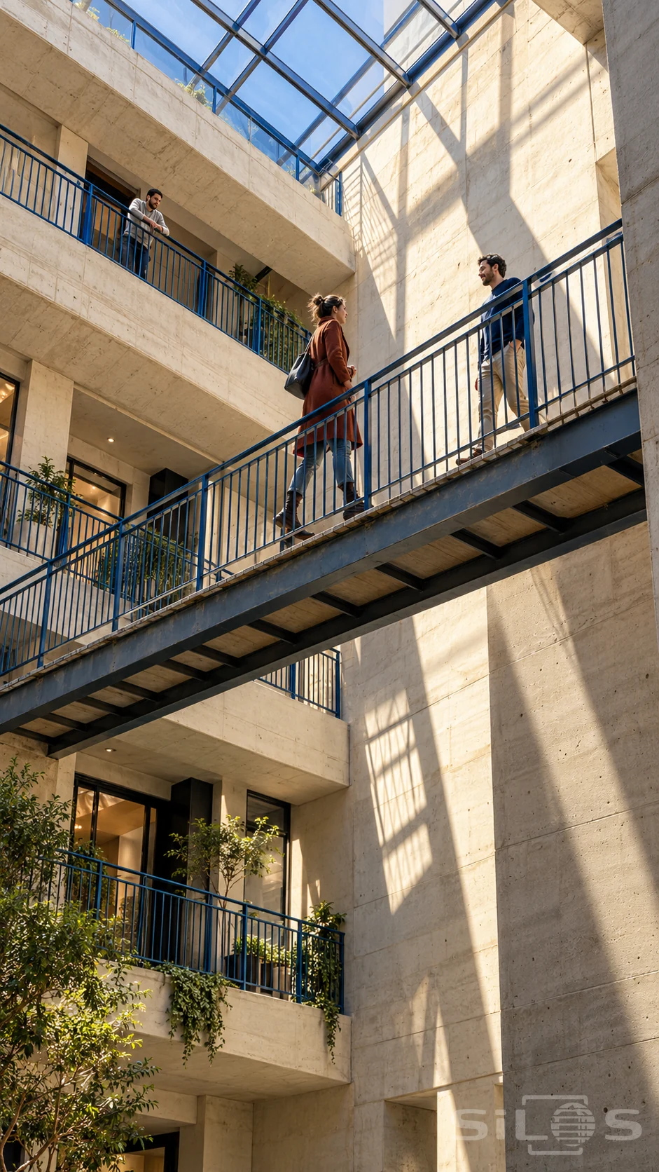 Two adults meet on a blue metal footbridge within a tall pale-concrete residential atrium while a third adult watches from an upper balcony.